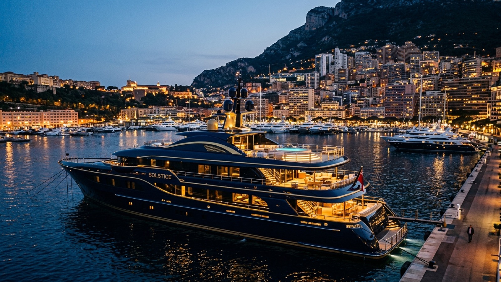 Superyachts berthed stern-to in Monaco's Port Hercule at dusk with Monte-Carlo behind